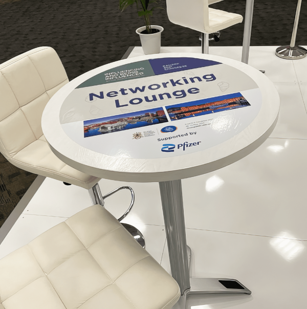 Round White Tabletop Carries A Networking Lounge Graphic And Small Sponsor Logos.