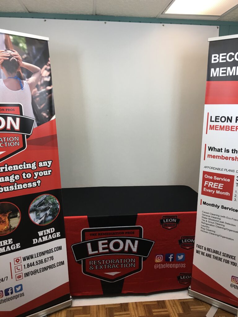 Leon Restoration And Extraction Display With Two Red-And-White Retractable Banners And A Matching Branded Event Counter.
