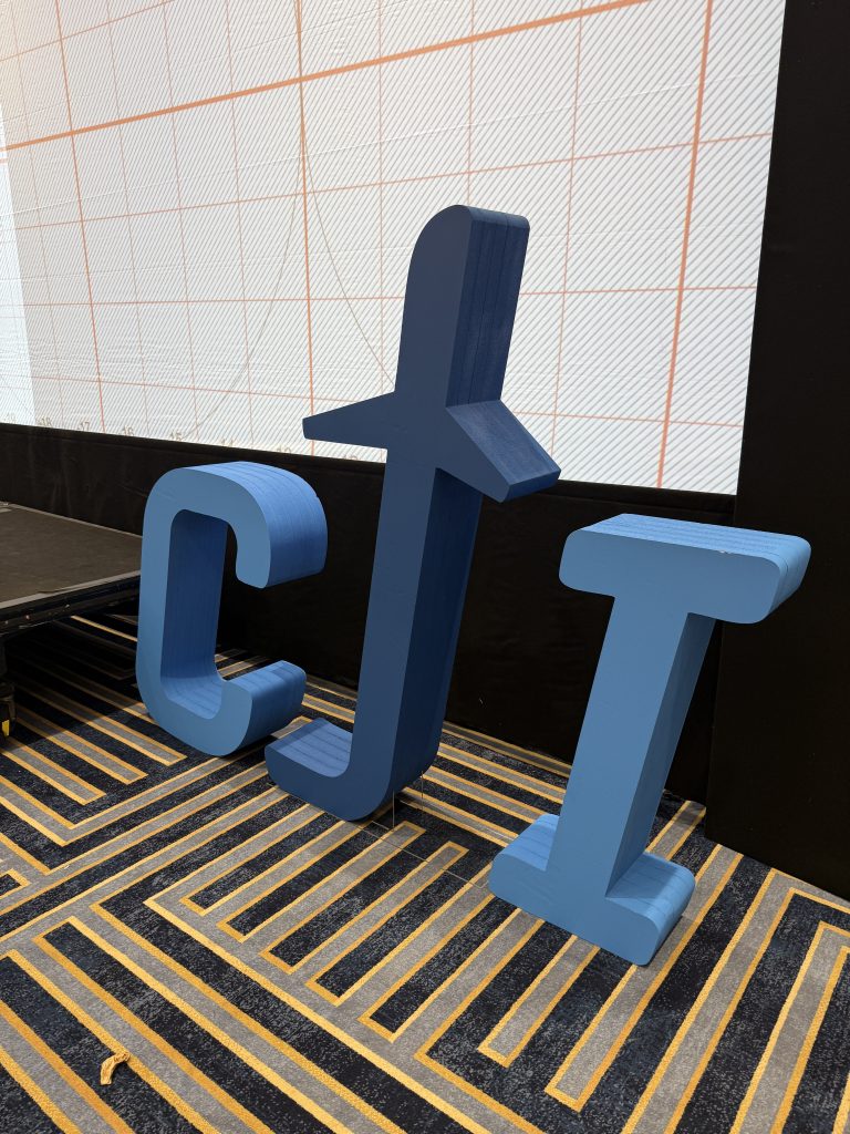 Blue Cji Standing Foam Letters Beside An Led Backdrop