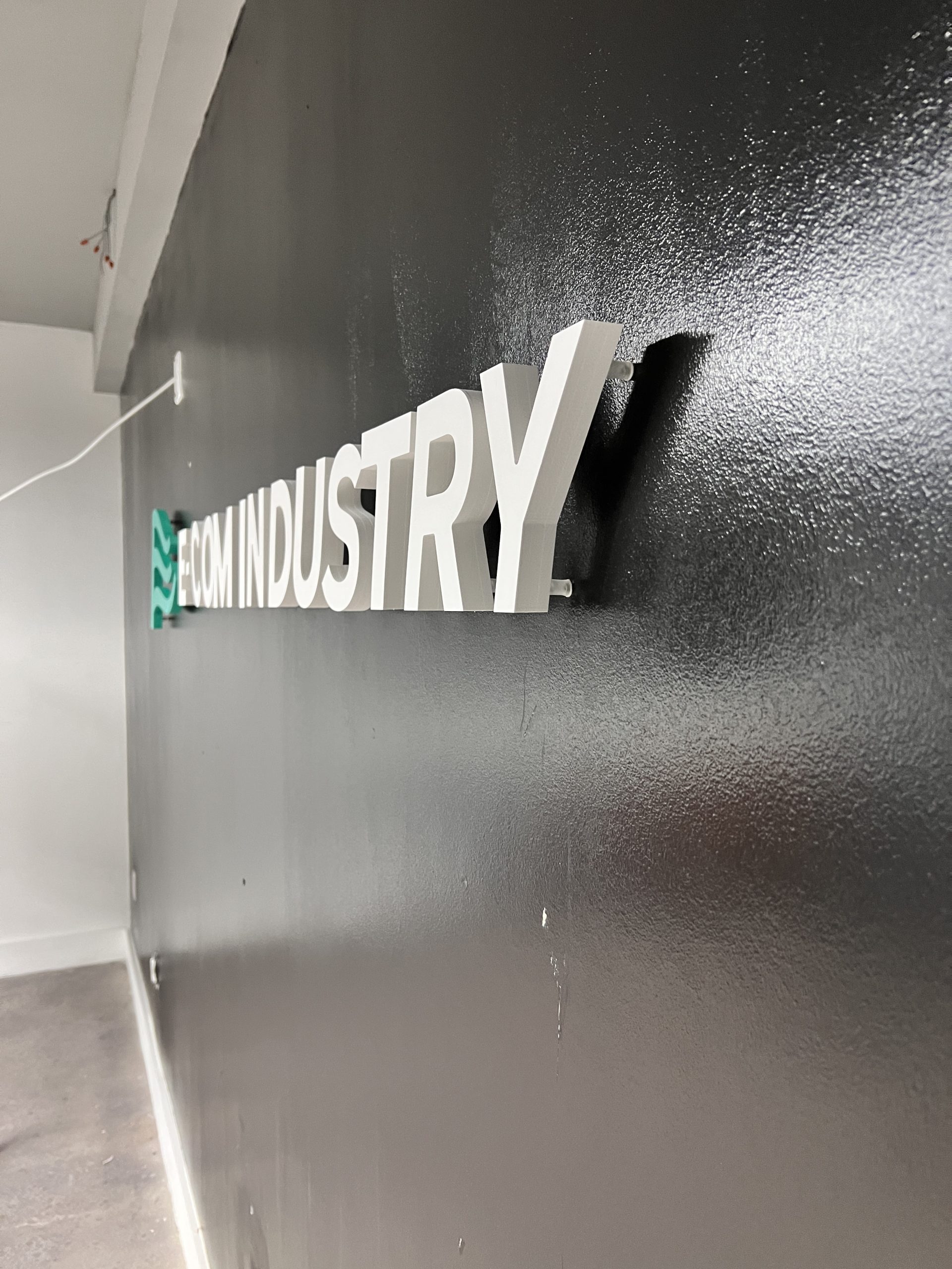 Doral Office Signage And Frosted Glass Graphics | E-Com Industry Side-Angle Close-Up Of Raised White E-Com Industry Pvc Letters Showing The 1-Inch Dimensional Profile On A Dark Wall
