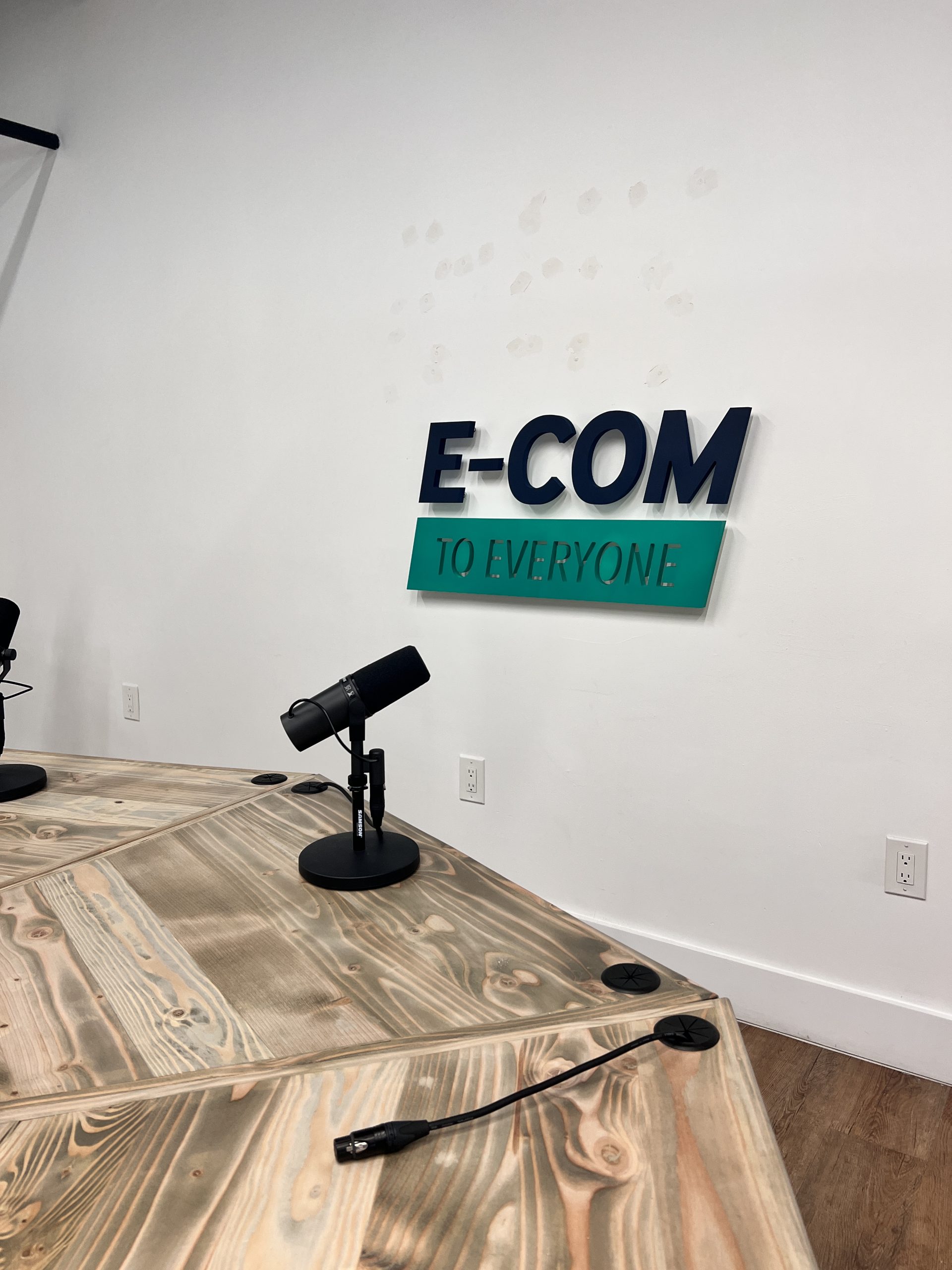 Doral Office Signage And Frosted Glass Graphics | E-Com Industry E-Com And To Everyone 1-Inch Pvc Sign Above A Podcast Studio Table With A Microphone