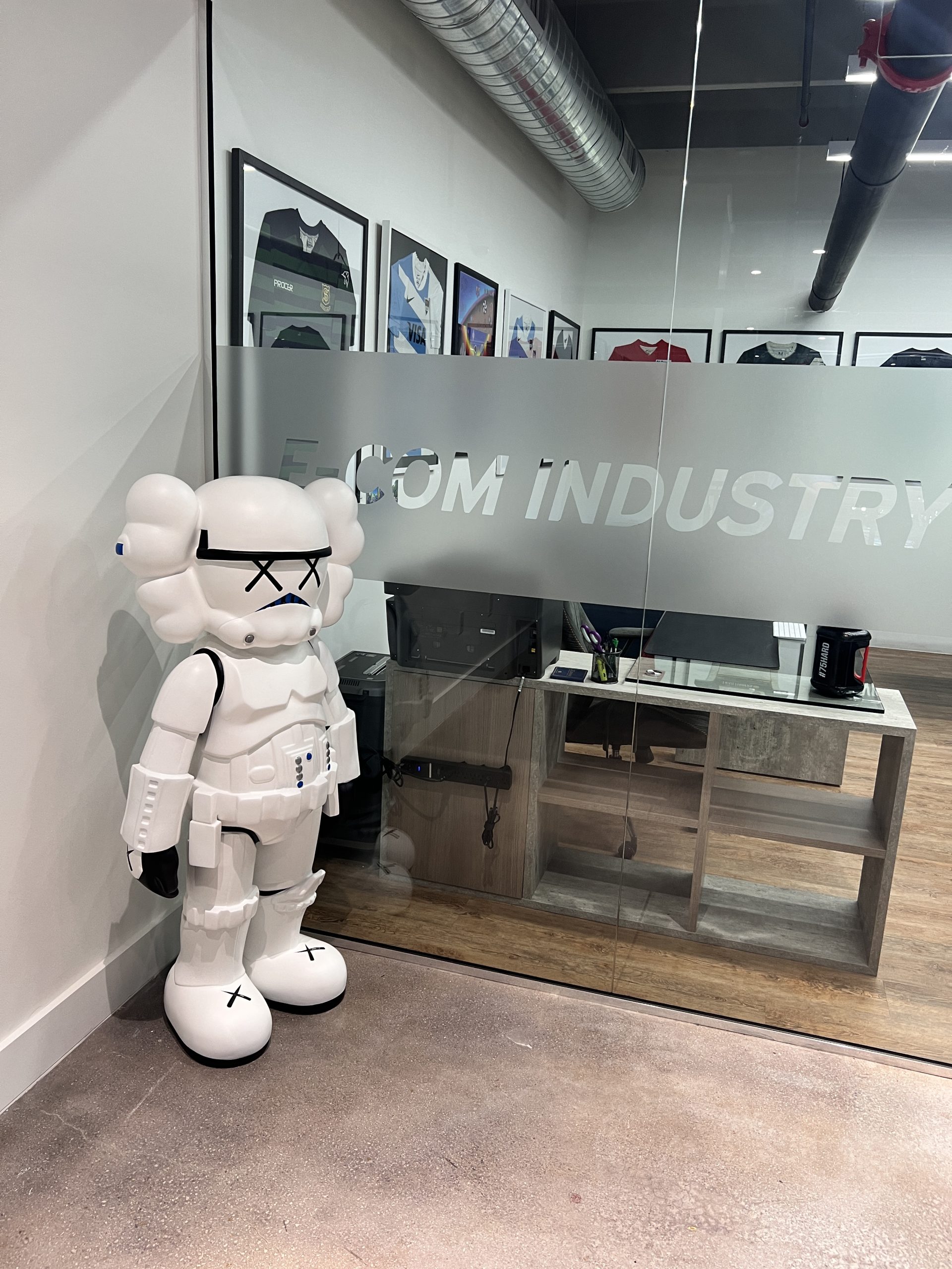 Doral Office Signage And Frosted Glass Graphics | E-Com Industry Frosted Glass Wall With E-Com Industry Lettering And Logo Graphics Beside A White Display Figure