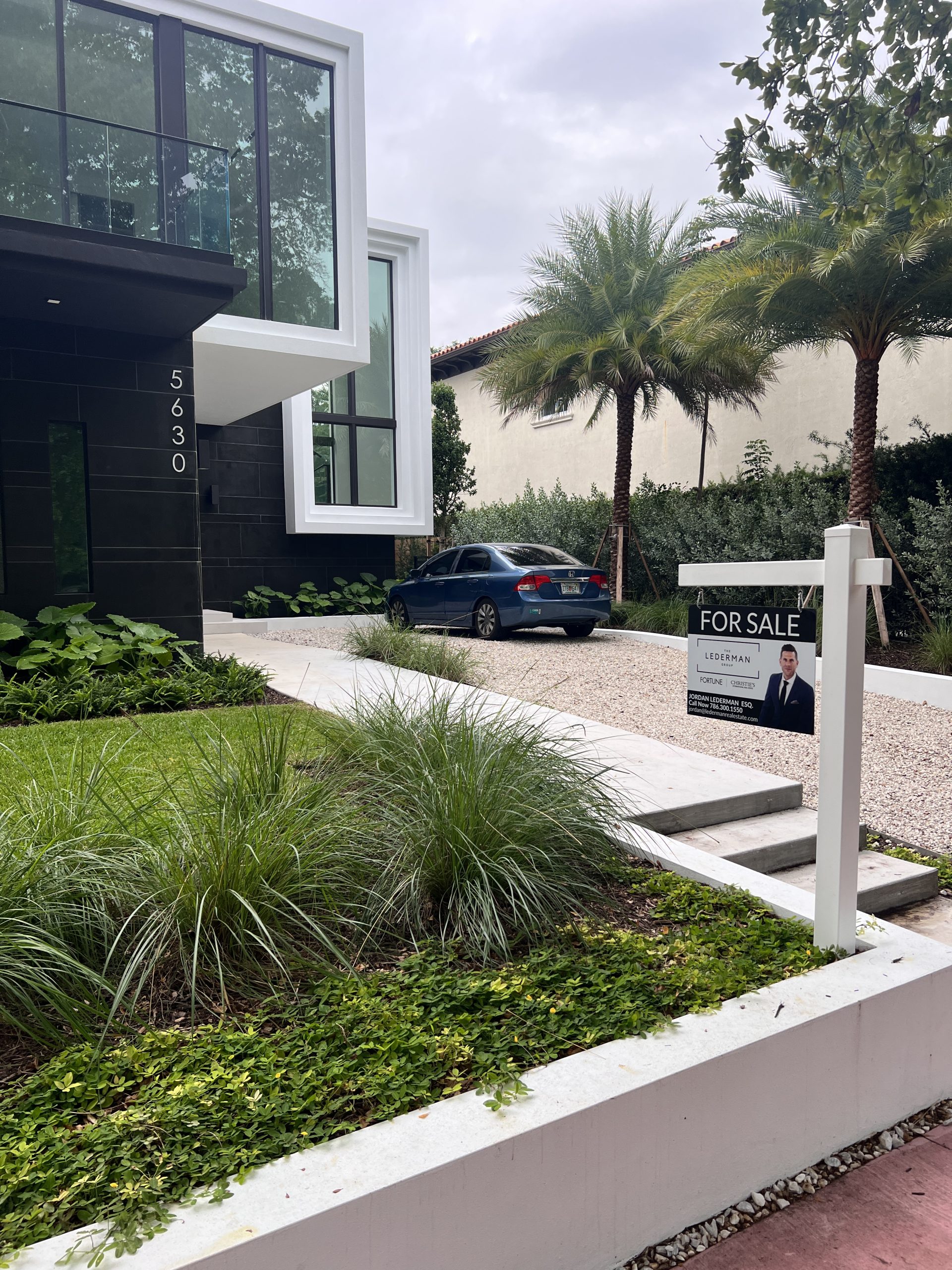 Vinyl real estate for-sale sign on a white post kit outside a modern Miami Beach property