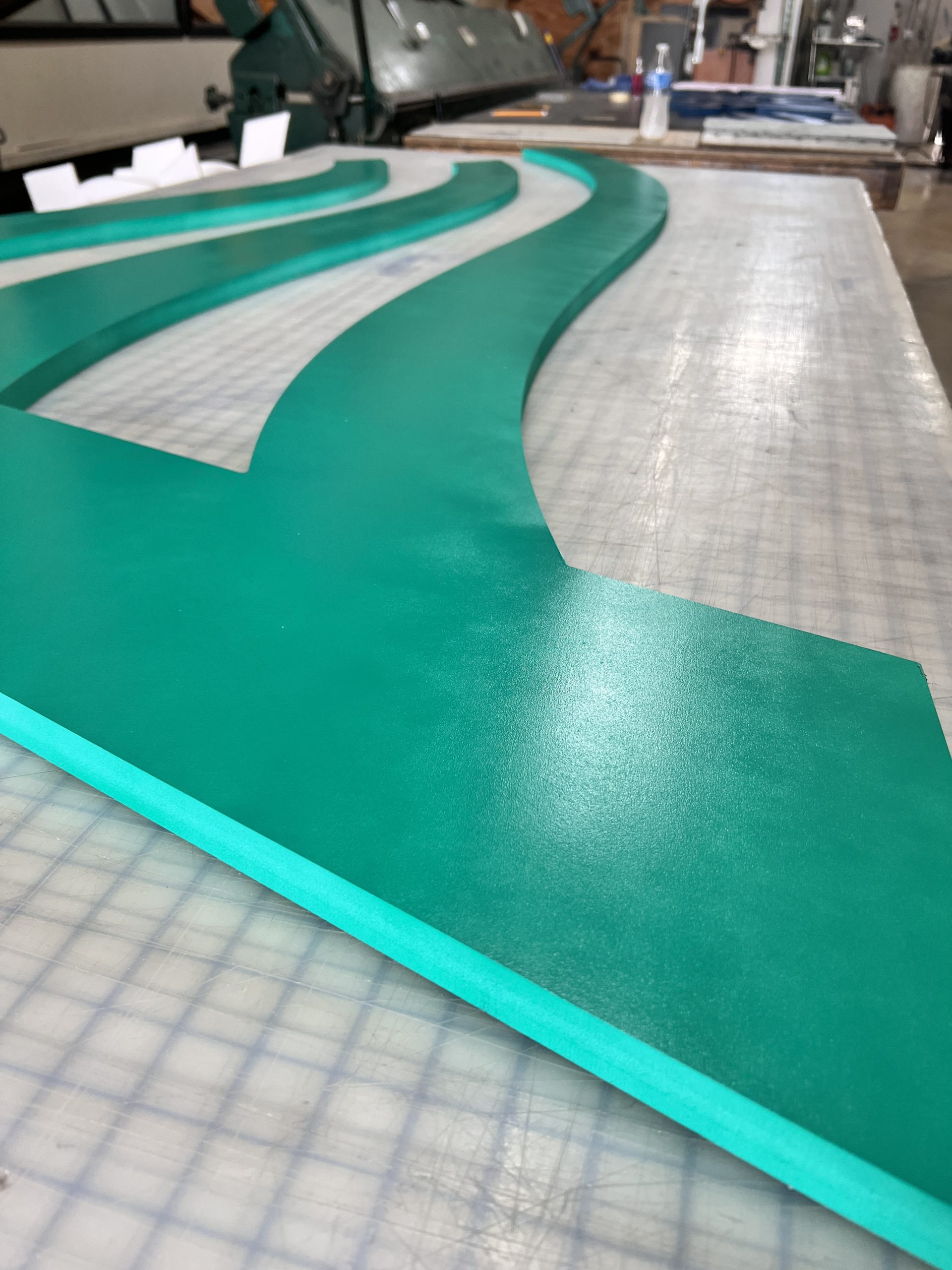 Doral Office Signage And Frosted Glass Graphics | E-Com Industry Teal Pvc Wave Logo Pieces Arranged On A Fabrication Table Before Installation