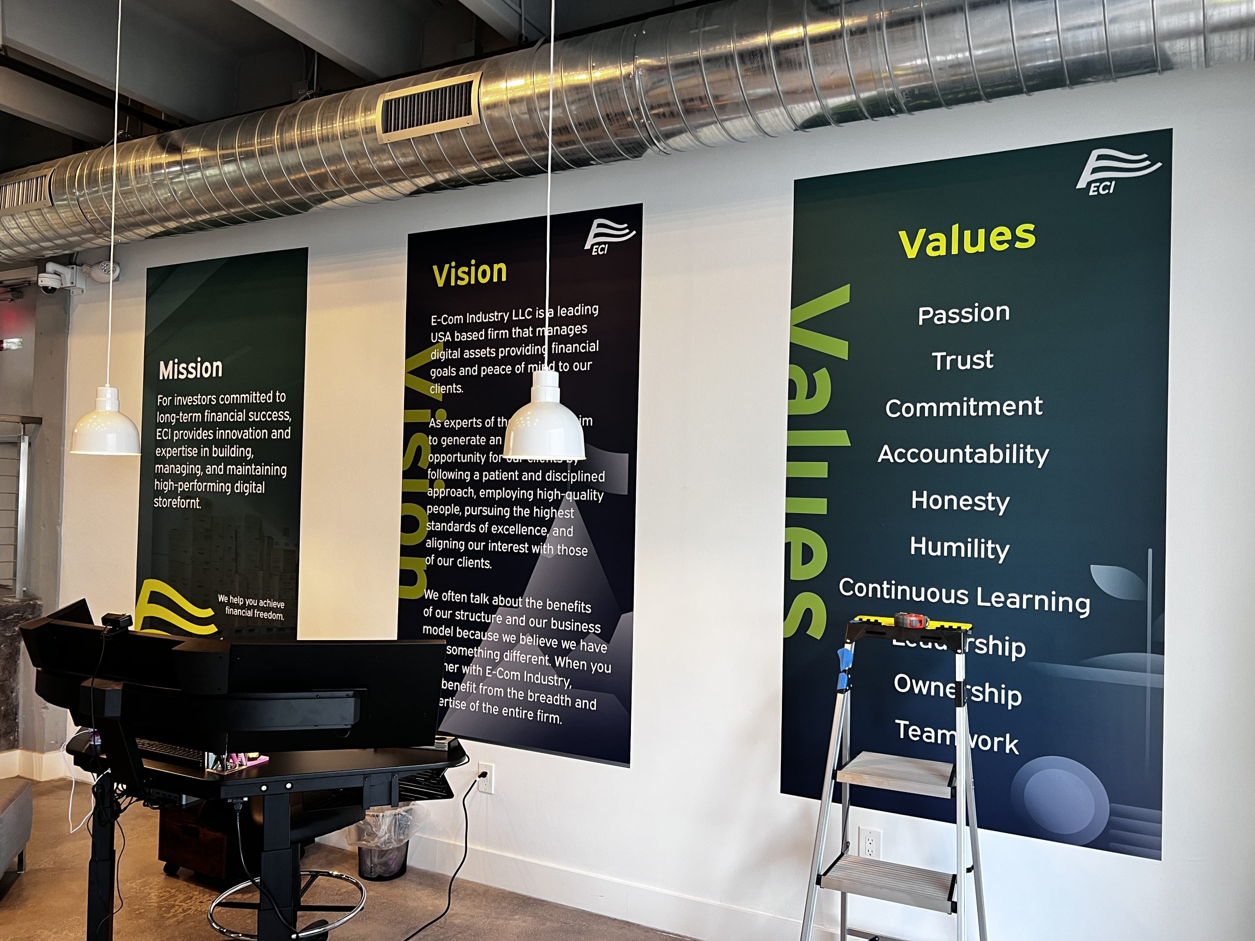 Doral Office Signage And Frosted Glass Graphics | E-Com Industry E-Com Industry Lobby Wall Panels Presenting Mission, Vision, And Values Graphics Beneath Exposed Ductwork