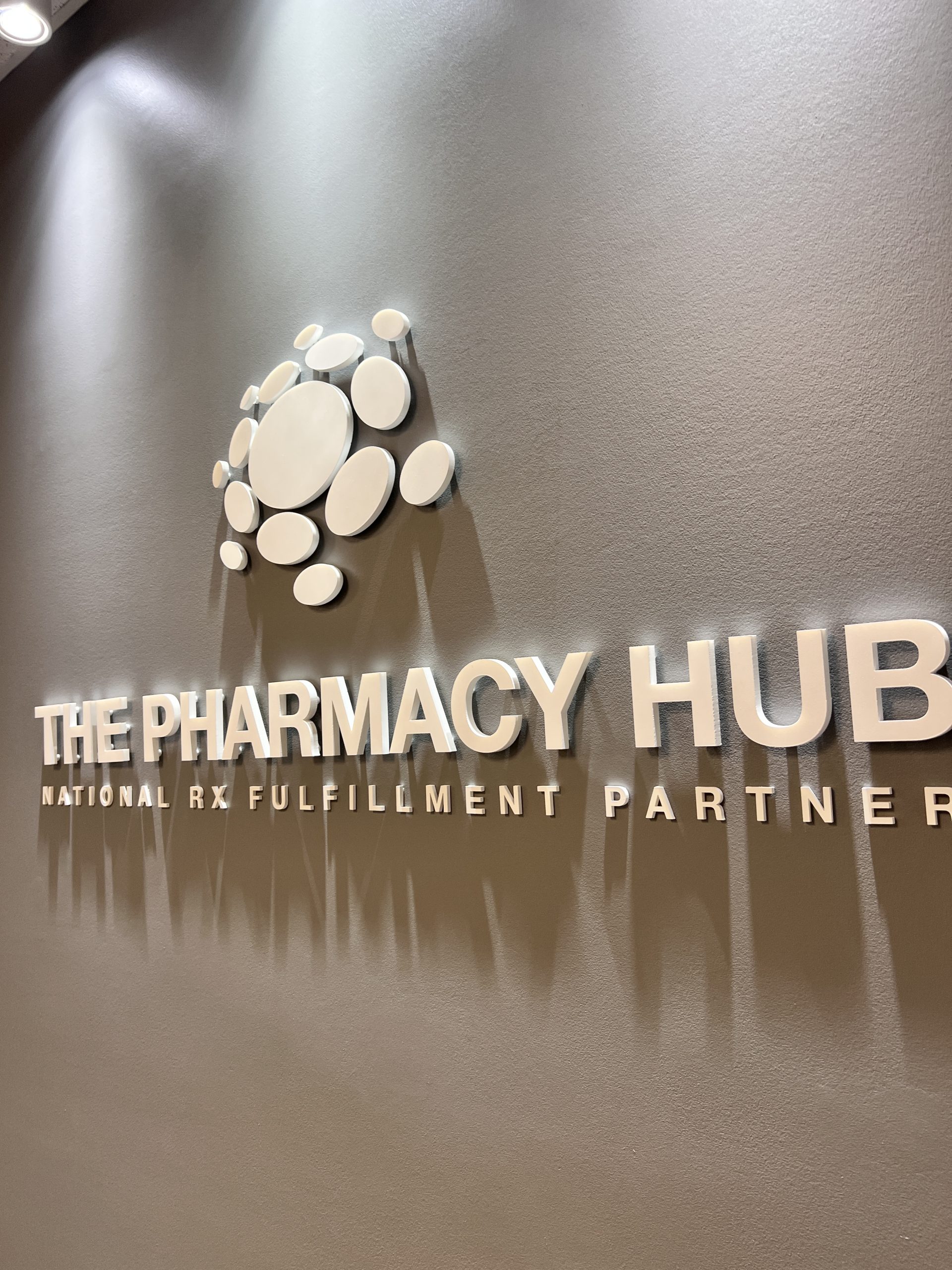 The Pharmacy Hub Pharmacy Signage In Miami Gardens Close-Up Of Raised White Acrylic Logo Elements And Dimensional Lettering On A Dark Gray Wall